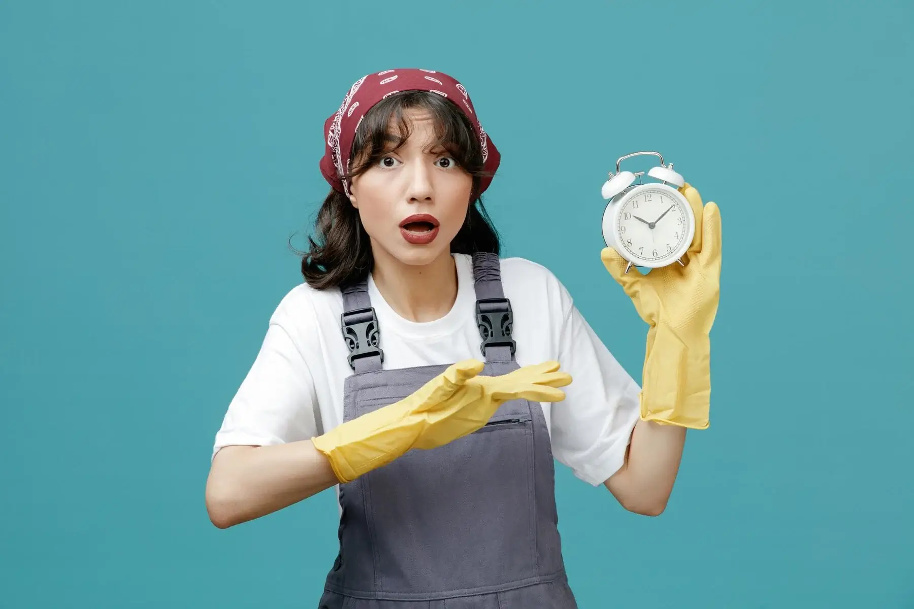 impressed-young-female-cleaner-wearing-uniform-bandana-rubber-gloves-showing-alarm-clock-looking-camera-pointing-with-hand-clock-isolated-blue-background_141793-135913 Female cleaner in uniform holding an alarm clock and pointing at it on blue background