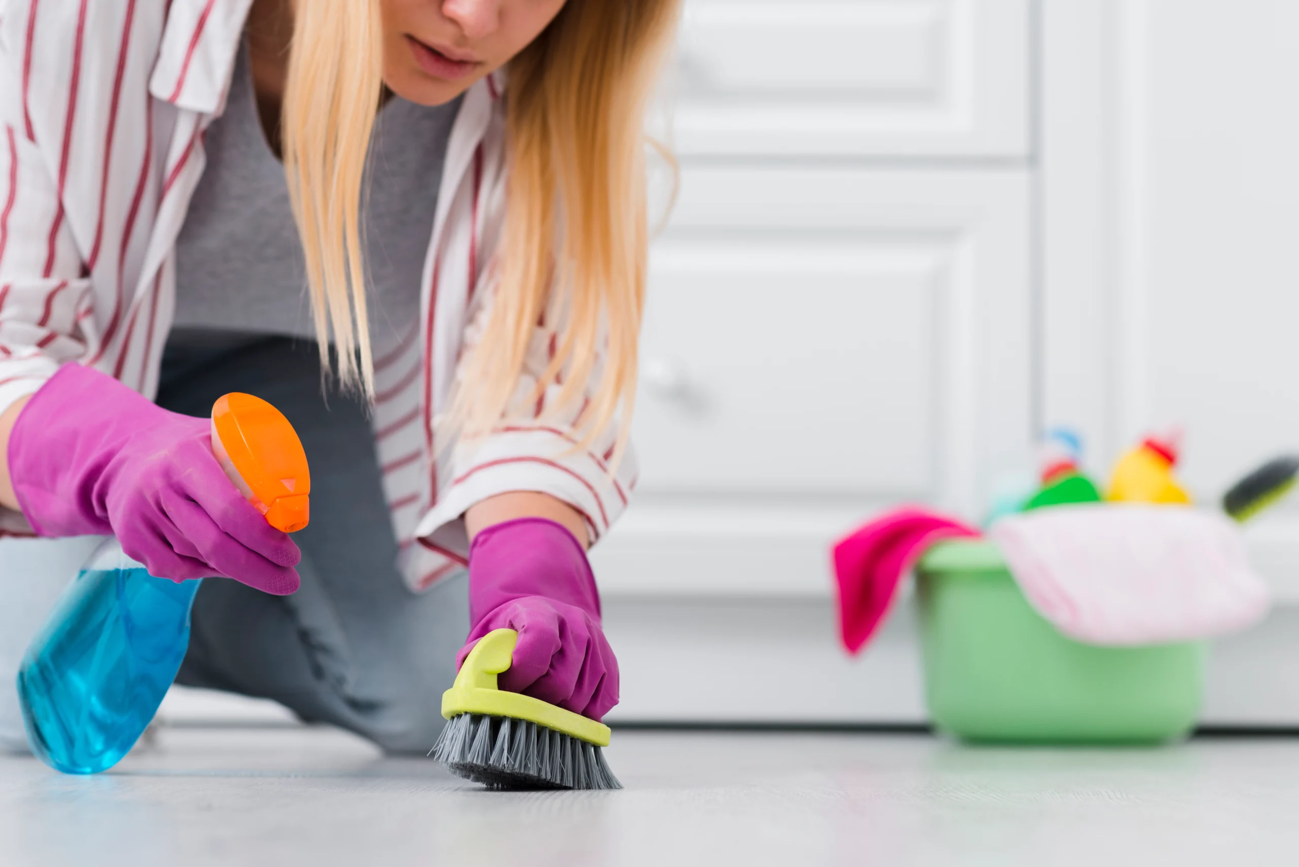 Woman scrubbing the floor with a brush and cleaning solution.
