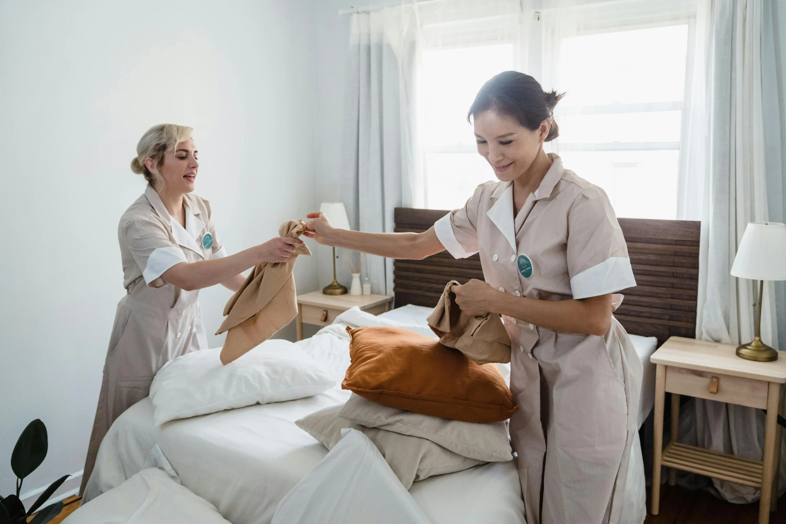Professional cleaners changing bedsheets in a clean and organized bedroom.