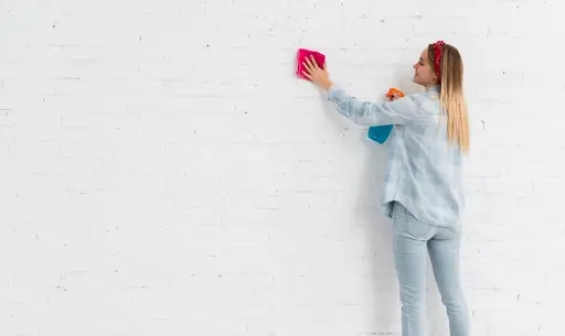 Wall washing in deep cleaning a wall with a sponge, wearing gloves, showing a close-up of the cleaning action.